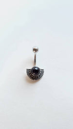 Introducing the Silver Belly Piercing by Kaya Movement. This exquisite belly button ring features a mother of pearl nacre design, resembling an ornate fan shape with a central black gemstone, making it perfect for your navel piercing. The jewelry is elegantly set against a pristine white background, showcasing its stunning craftsmanship.