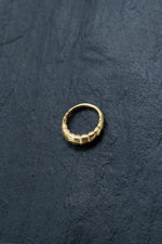 A close-up image of a Biomechanical - 18k Gold Septum 10mm by Kaya Movement on a dark, textured surface. The nose ring features a unique geometric design with adjoining hexagonal shapes, reminiscent of cybernetic bio-organic jewelry.