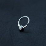 A small, silver 8mm septum ring by Kaya Movement, featuring an opal stone set in the center, is placed on a textured black surface. The opal exhibits iridescent colors, adding a vibrant touch to the minimalist design. This opal nose ring is perfect for those who appreciate subtle yet striking accessories.
