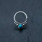 A striking piece from Kaya Movement, the silver septum ring with turquoise is a standout on a dark textured surface. Featuring a central turquoise gemstone flanked by small silver beads, this simple yet elegant Bohemian jewelry gift effortlessly draws attention to the vivid blue hue of the stone. Perfect as a cartilage earring, daith piercing, or helix piercing.