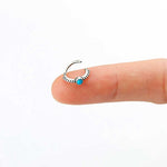A close-up of a finger holding the Kaya Movement 925 silver Indian nose ring, featuring a central blue Turquoise gemstone. The semi-circular design is intricately detailed with textured patterns surrounding the stone. Set against a plain white background, this versatile piece can be used as an 8mm septum ring, silver nose hoop, Rook piercing jewelry, Tragus piercing accessory, or Helix jewelry.