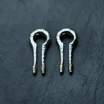 Two traditional jaw harps with textured metal designs are placed side by side on a dark, textured surface. Each harp has a looped structure with a straight, narrow tongue extending from the base, showcasing intricate craftsmanship that is reminiscent of the detailed work found in Kaya Movement's Silver White Brass Ear Weights for stretched lobes body mod jewelry.