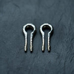 Two shiny metallic harp picks with intricate patterns displayed on a dark textured surface resemble the elegant Silver White Brass Ear Weights from Kaya Movement. The picks are identical and symmetrically positioned side by side, evoking the precision of body mod jewelry designed for stretched lobes.