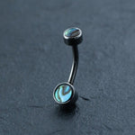 The Kaya Movement Belly Button Jewelry Hypoallergenic Navel Rings feature a curved barbell design with two small round ends adorned with abalone shell inlays. This Boho-Chic style piece boasts a metallic, dark-colored finish and is showcased on a dark, textured background. Crafted from Surgical Steel 316L, it perfectly combines durability with an elegant design.