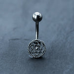 Introducing the Silver Mandala Belly Button Rings by Kaya Movement—a stunning surgical steel navel piercing boasting a 9mm curved barbell with an intricate flower-like mandala design at the center. Adorned with delicate bead details around the edges, this boho belly ring is perfect for navel piercings and stands out beautifully against a textured dark gray surface.
