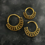 Three gold-plated brass nose rings from Kaya Movement's Gold-Plated Brass Septum in Maya Tribal Design collection are arranged on a dark, textured surface. The two smaller rings are positioned upside down, while the larger one sits on the left side. Exhibiting an intricate geometric style typical of tribal jewelry, this set reflects the cultural artistry reminiscent of Maya traditions.