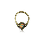 A small brass nose ring with a gold-colored finish, featuring an iridescent opal encased in a decorative setting adorned with bead-like details. The circular Opal Bohemian Septum Ring by Kaya Movement has an opening at the bottom and is photographed against a plain white background.