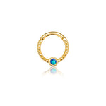 The Oriel Minimalist Gold PVD 316L Stainless Steel Septum with Blue Opal by Kaya Movement is a sleek circular septum featuring a textured beads pattern on the lower half, highlighted by a small round blue opal encased in gold at the bottom center. This subtle yet elegant nose, tragus, or lobe jewelry piece is presented on a white background with a slight reflection beneath it.