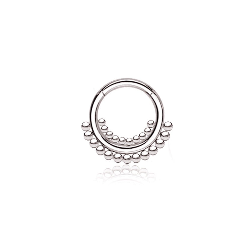 The "Bohra" septum jewelry from Kaya Movement features a delicate, silver circular design made of 316L steel. It showcases minimalist elegance with a larger circular form adorned with evenly spaced small balls along the bottom half. The septum has a polished, reflective surface and an open design at the top, measuring 1.2mm in gauge and 8mm in diameter.