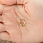 A hand holds the Liora Minimalist Mandala-Inspired Septum in 316L Steel Gold Finish by Kaya Movement. The band, with a gauge of 1.2mm and available in diameters of 6mm, 8mm, and 10mm, features an intricate design inspired by mandalas. The background is slightly blurred, highlighting the delicate details against the palm.