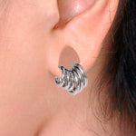 Close-up of an ear adorned with the Aurel Simple Ear Ring in 316L Steel silver finish by Kaya Movement, which wraps around the earlobe in a spiral design, creating a layered effect akin to stacking rings. The background is out of focus, emphasizing the minimalist elegance of this jewelry piece available in gauges 2 or 3mm and diameters of 8, 10, 12, and 14mm.
