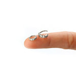 A close-up of a hand with the index finger extended, balancing two small LONA Silver Mandala-Style Septum rings by Kaya Movement, featuring a jagged star design on the outer edge. The background is a plain white.