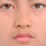 Close-up of a person's face, focusing on their nose with the Lysa Elegant Design Septum from Kaya Movement. The person's skin is smooth, and their eyes are brown. The gold septum ring features a delicate chain design and adds a subtle shine for everyday elegance. The lips are slightly parted, and minimal makeup is worn.