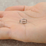 A hand holding a sleek gold PVD "Trion" septum ring by Kaya Movement rests on the palm. The minimalist 316L steel piece, featuring a triple ring effect with parallel bands connected at the ends, is sharply focused against a slightly blurred background.