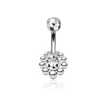 The Zirka Navel Jewelry from Kaya Movement, crafted from 316L surgical steel, features a larger central clear zircon surrounded by small silver beads in a circular pattern. Another smaller clear gemstone adorns the top of the curved silver bar. This Boho Essence navel jewelry, reflecting natural and bohemian elegance, is positioned against a white background.