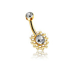 The Lustra Navel Piercing by Kaya Movement epitomizes contemporary elegance with its geometric design and radiant zircon gems. This gold-finished stainless steel belly button ring features a small, round clear gem at the curved bar and a larger oval clear gem surrounded by a cluster of small gold beads at the bottom. The piece is showcased on a white background, accentuated by a subtle reflection beneath it.