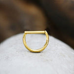 Close-up of a minimalist gold geometric ring placed on a smooth stone. The Anneau Segmenté Doré Minimalist from Kaya Movement features a unique design with a flat top bar connecting the sides, forming a semicircle. The background is softly blurred, emphasizing the ring's details.