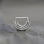 A close-up shot of the elegant, minimalist Anneau de Septum Argent from Kaya Movement, featuring a geometric design with triple-stacked semi-circular bands. Crafted from premium surgical steel, this 8mm hypoallergenic and lightweight septum ring rests on a smooth, slightly textured surface, showcasing its modern and sophisticated style.