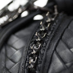 Close-up image of the APOPHIS Post-Apocalyptic Leather Shoulder & Belt Bag by Kaya Movement, showcasing its black quilted leather with interwoven detailed stitching and several small, shiny metallic anchor-shaped embellishments arranged in a row. The texture of the leather and intricate design elements make it a perfect wasteland festival accessory.