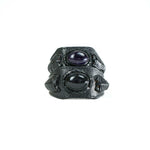 A close-up of the ANOM Men's Black Cuff Leather Bracelet by Kaya Movement, featuring an oval-shaped, dark purple genuine Amethyst gemstone and a round, black stone, with intricate textured detailing along the band, set against a plain white background.