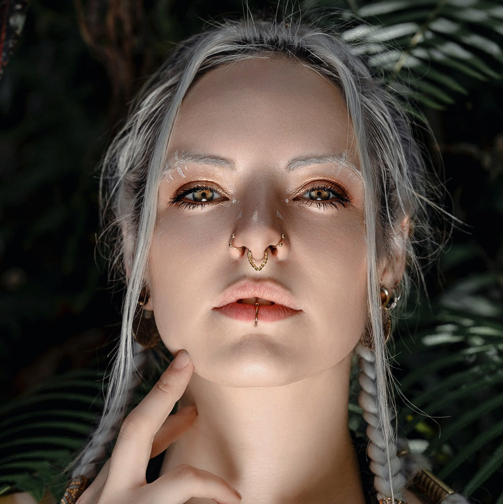 Close-up portrait of a person with platinum blonde hair against a green leafy background.