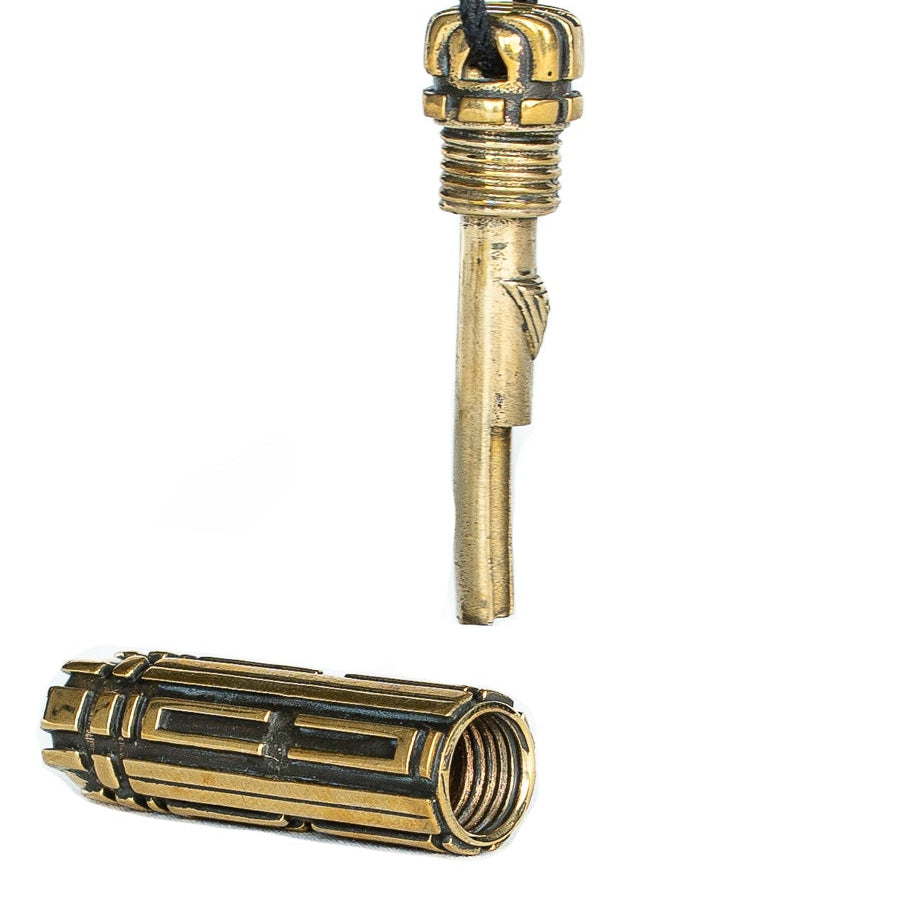 A brass cylindrical pendant with a futuristic, biomechanical design, suspended from a black cord. The pendant is partially open, revealing a hidden inner mechanism.