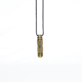 A brass pendant with a symmetrical sci-fi design, hanging vertically from a black cord in a minimalistic setting.