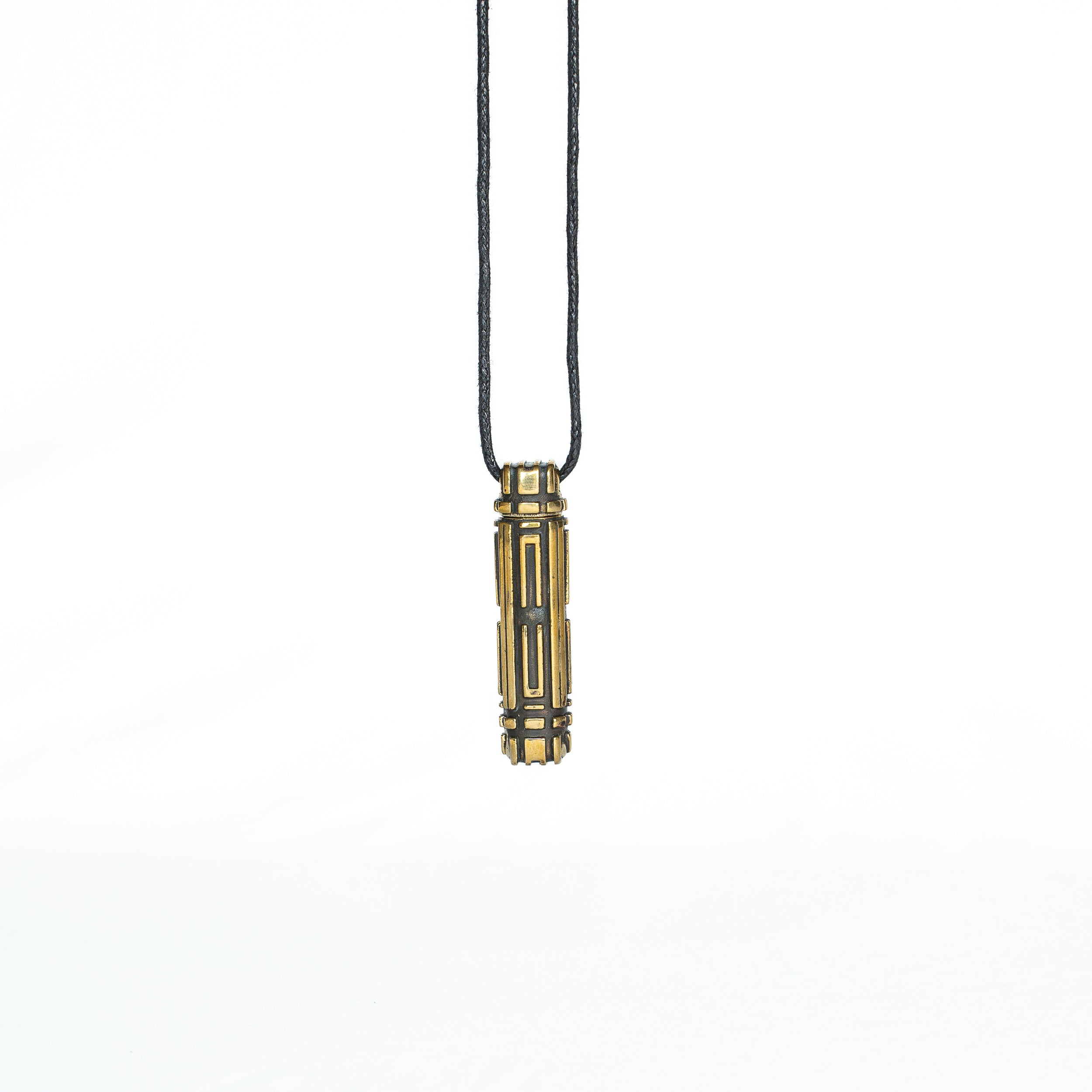A brass pendant with a symmetrical sci-fi design, hanging vertically from a black cord in a minimalistic setting.
