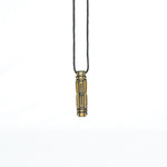 A brass pendant with a symmetrical sci-fi design, hanging vertically from a black cord in a minimalistic setting.