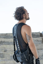 Back view of a black leather double pouch holster bag with adjustable studded straps, worn over a mesh tank top.