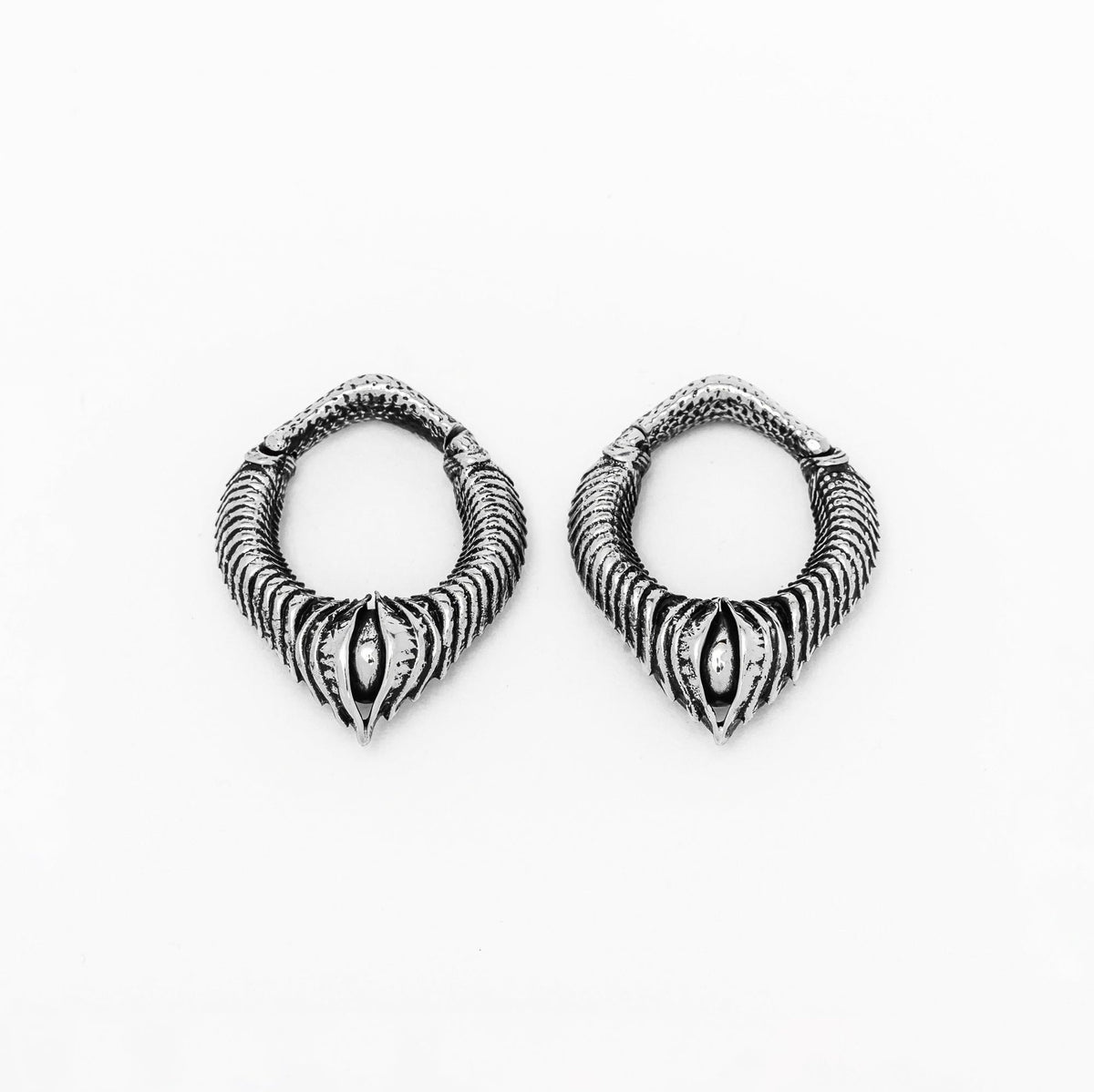 The MARVDASHT Small Biomechanical Clicker Ear Weights in Silver Brass from Kaya Movement are a pair of intricately designed hoop earrings featuring a twisted, rope-like pattern and an ornate central bead. These eye-catching earrings blend vintage and modern aesthetics, evoking a hint of post-apocalyptic body jewelry, and are displayed on a plain white background.