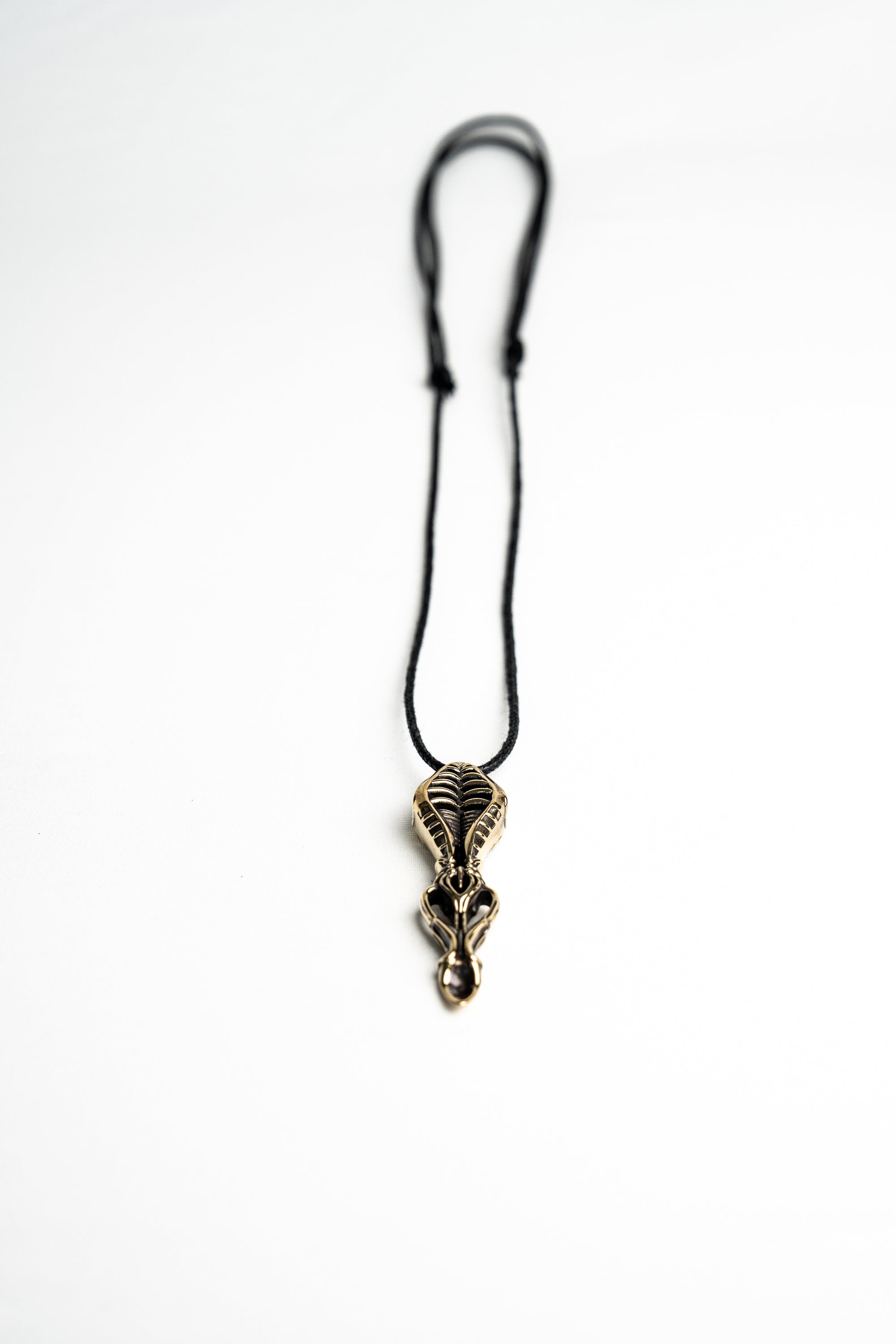 Artistic shot of the biomechanical pendant laying on a white background, emphasizing its sculptural and industrial style