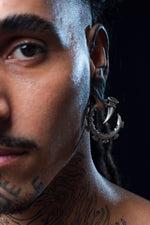 Close-up of an individual wearing GIGER Biomechanical Open Ended Hoop Ear Weights in silver by Kaya Movement. The intricate biomechanical design is showcased in the stretched earlobe, blending seamlessly with the person bold geometric tattoos.