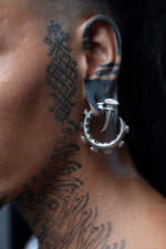 Close-up of an individual ear wearing GIGER Biomechanical Open Ended Hoop Ear Weights in silver by Kaya Movement. The intricate design blends seamlessly with bold geometric tattoos, creating a unique fusion of tribal and futuristic aesthetics.