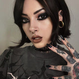 Side profile of a tattooed model wearing a biomechanical gold septum clicker and stretched ear plugs. Her piercing gaze and gothic-inspired attire enhance the post-apocalyptic fashion look.