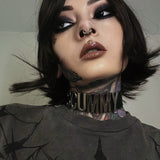 Close-up portrait of a tattooed woman with intense eye makeup, a cybernetic gold septum ring, and a bold black choker. Her alternative style embodies a dark futuristic aesthetic.
