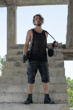 Model standing confidently on concrete steps, holding a black leather double pouch holster bag with hand-carved spine details, dressed in black alternative wear.