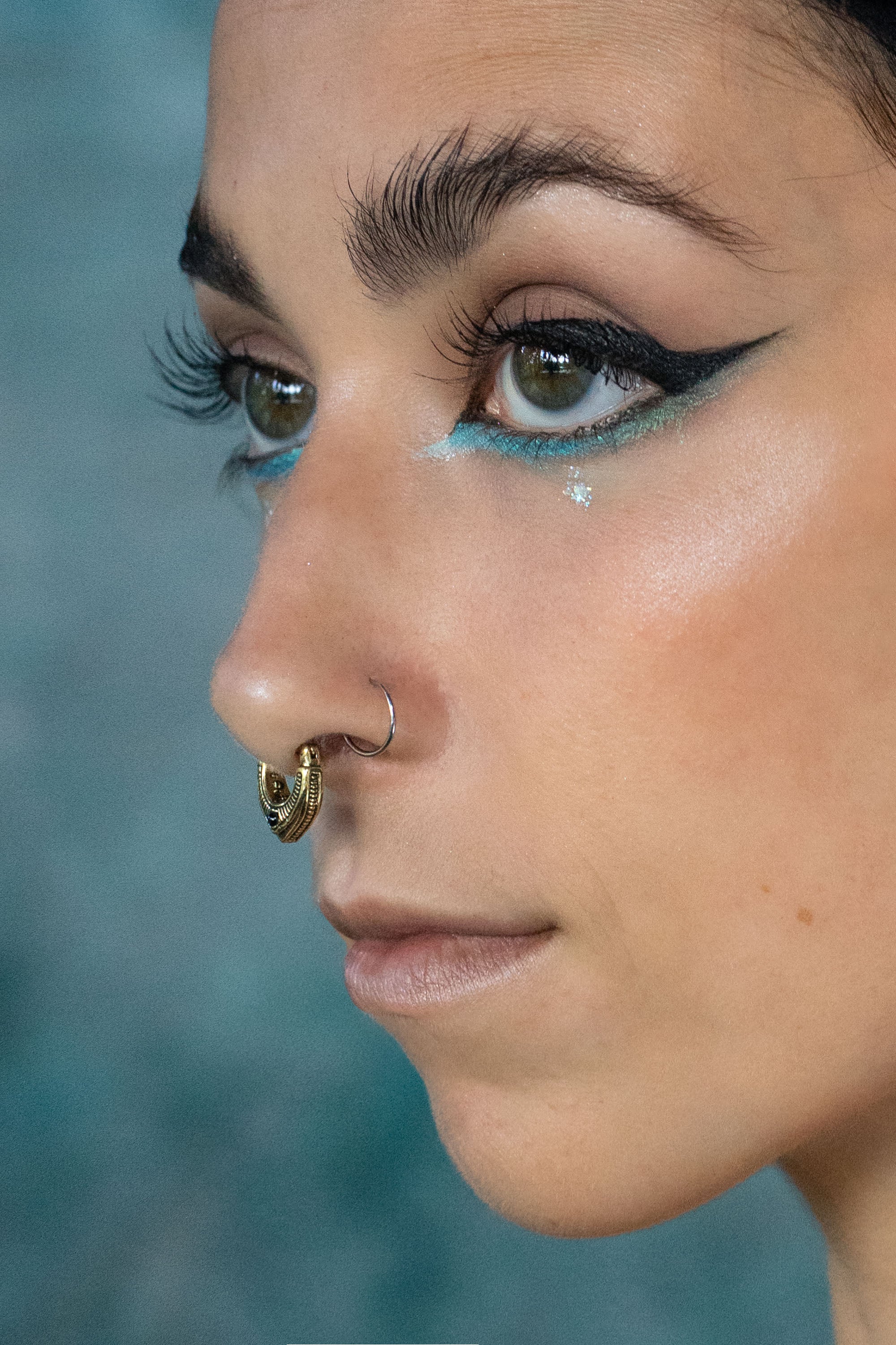 Close up artistic shoot of a women with green eyes, wearing a gold septum clicker with garnet stone