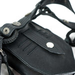 A close-up of the KERO Unisex Lightweight Leather Holster Bag by Kaya Movement reveals a black sheep skin leather strap adorned with metal snaps and eyelets, reminiscent of a post-apocalyptic harness. The strap features intricate stitching and braided leather details, with its texture standing out and the metal accents providing a striking contrast.