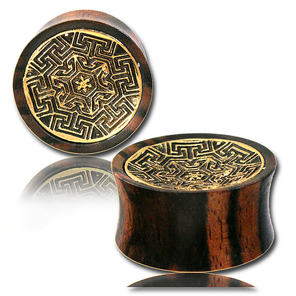 Two MAYA Round Saddle Plugs in Gold & Wood by Kaya Movement, featuring intricate golden geometric designs on the front. The wooden gauges are rounded with a slightly concave shape and a smooth, dark brown finish. The reflective surface beneath them shows a faint mirror image of the plugs. Available in sizes from 12mm to 25mm gauge.