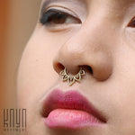 Close-up of a person's face showcasing a MAWAR Lotus Flower Septum Ring in Gold from Kaya Movement, crafted in 18 gauge gold brass body jewelry. The person's lips are painted bright pink, and their eyes are closed. In the bottom left corner, a logo with the text "Kaya Movement" is visible.