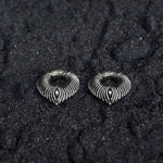A pair of MARVDASHT Medium Cyborg Clicker Ear Weights in 925 Silver from Kaya Movement, shaped like hearts with intricate ridged patterns, placed on a textured black surface. These silver ear weights have a symmetrical, layered design that creates a striking visual contrast against the dark background.