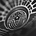 Close-up of an intricate black and white design resembling tribal or Aztec art. The pattern features bold, abstract geometric shapes and lines forming a circular motif with symmetrical elements radiating outward, reminiscent of the ornate CROP CIRCLE Oversized Tribal Disc Hoop Earrings in Silver (16 gauge) by Kaya Movement. The texture appears to be etched or carved.