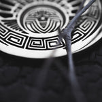Close-up image of the CROP CIRCLE Oversized Tribal Disc Hoop Earrings in Silver by Kaya Movement, featuring intricate, symmetrical geometric patterns and a central motif resembling an eye. Twigs partially obstruct the view, drawing attention to the detailed craftsmanship of these 16 gauge boho earrings.