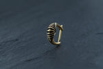 The DIARA Biomechanical Clicker Hoop Septum Nose Ring in Gold by Kaya Movement, featuring an elegant 16-gauge curved hoop with intricate shell-like design and detailed textures, is placed on a dark, smooth surface. This exquisitely crafted nose ring makes an exceptional addition to any unisex piercing collection.