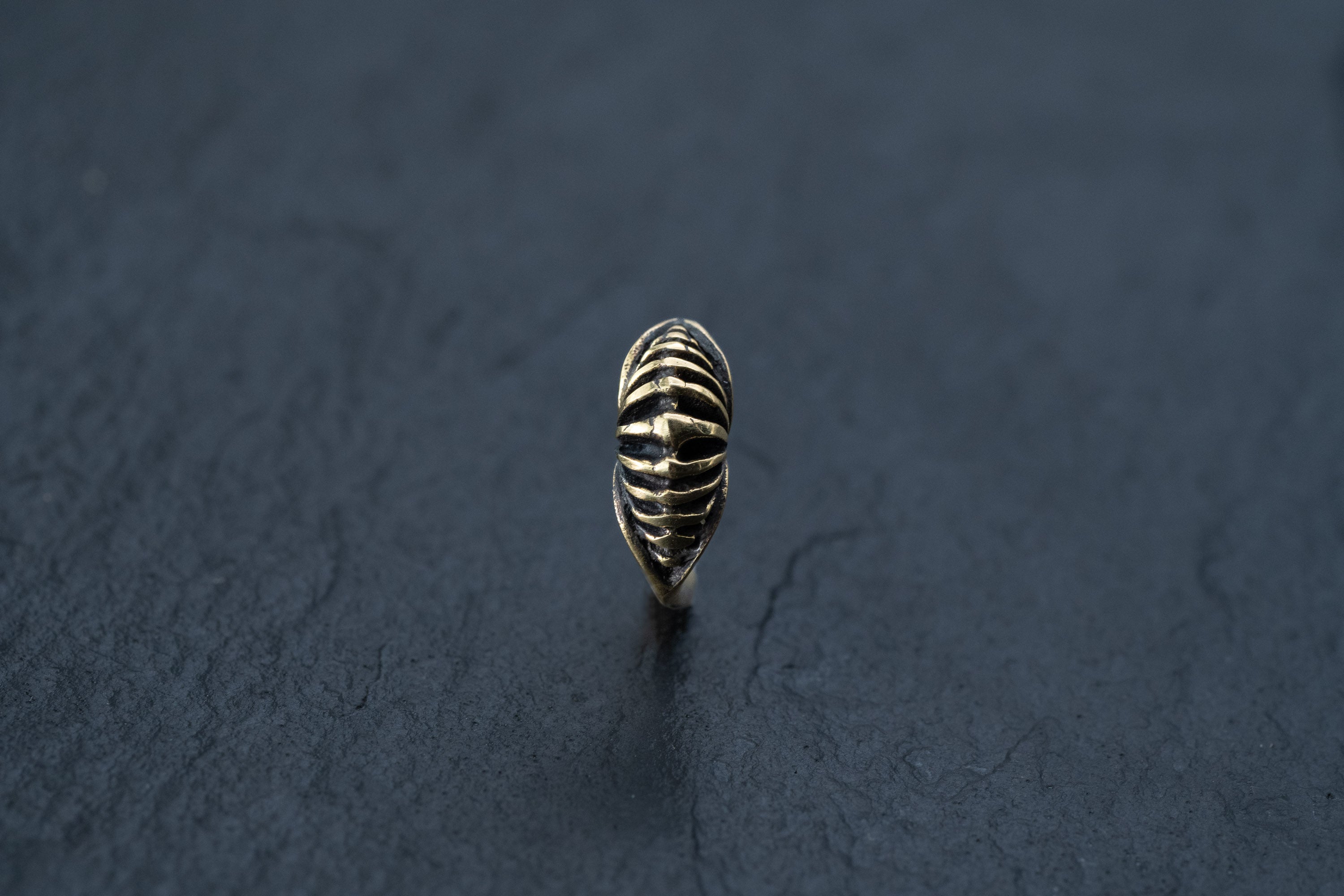 A close-up of the DIARA Biomechanical Clicker Hoop Septum Nose Ring in Gold by Kaya Movement, featuring an intricate, textured design reminiscent of a wrapped or coiled pattern. Set against a dark, textured background, the 16 gauge ring highlights its polished golden surface and detailed craftsmanship.