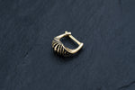 A close-up photograph of the Kaya Movement DIARA Biomechanical Clicker Hoop Septum Nose Ring in Gold, featuring a unique ribbed design and polished finish, placed on a dark, textured surface. The 16 gauge earring boasts an elegant hinged clasp, reminiscent of an exquisite cyborg clicker.