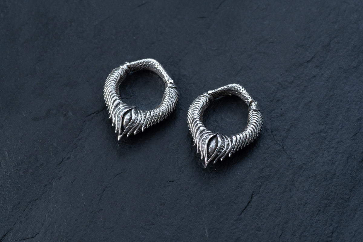 Introducing the MARVDASHT Small Biomechanical Clicker Ear Weights in 925 Silver by Kaya Movement, featuring a unique coiled design with pointed, claw-like ends that exude sci-fi vibes. These unisex 2 gauge earrings are presented on a dark, textured background.