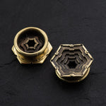 Close-up of two HEXA Futuristic Geometry Hexagon Flesh Tunnels in Gold by Kaya Movement, placed on a dark surface. One tunnel is positioned upright, displaying an intricate internal structure reminiscent of visionary AI plug earrings, while the other is laid flat, showcasing a multi-layered, symmetrical pattern.