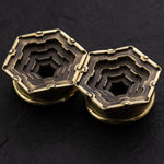 A close-up image of a pair of HEXA Futuristic Geometry Hexagon Flesh Tunnels in Gold, by Kaya Movement. The multi-layered geometric designs within the hexagonal shapes showcase intricate patterns, reminiscent of visionary AI plug earrings. Set against a dark background, the image highlights the metallic texture and craftsmanship of these 12mm to 24mm pieces.